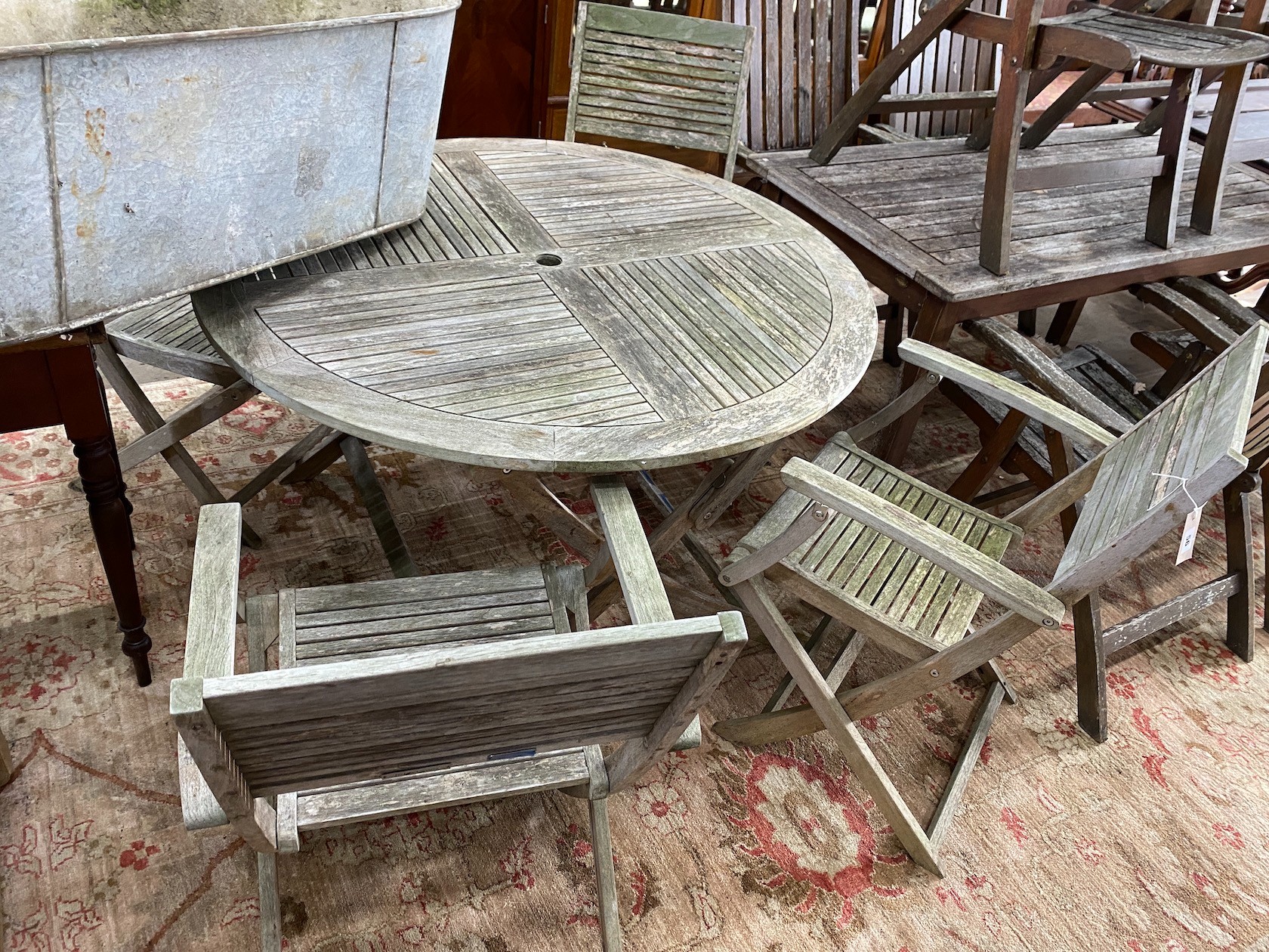 A John Lewis retailed weathered teak circular folding garden table, diameter 120cm, height 74cm and four folding elbow chairs, two with arms
